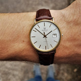 A wrist shot of a vintage Gold Marvin Revue watch with a date window at 3 o'clock, with a Italian Buffalo Grain Calf Leather strap in Brown.